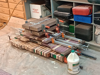 Bar clamps holding a laminated wood block together on a workbench with a jug of glue beside it
