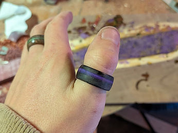 Two finished wooden rings worn on a hand, one with a purple resin fill and one with green