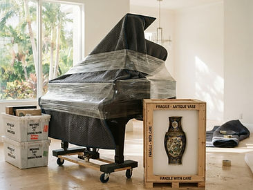 A grand piano wrapped in moving blankets and an ornate vase packed in a custom wooden crate with protective foam, ready for a specialty move