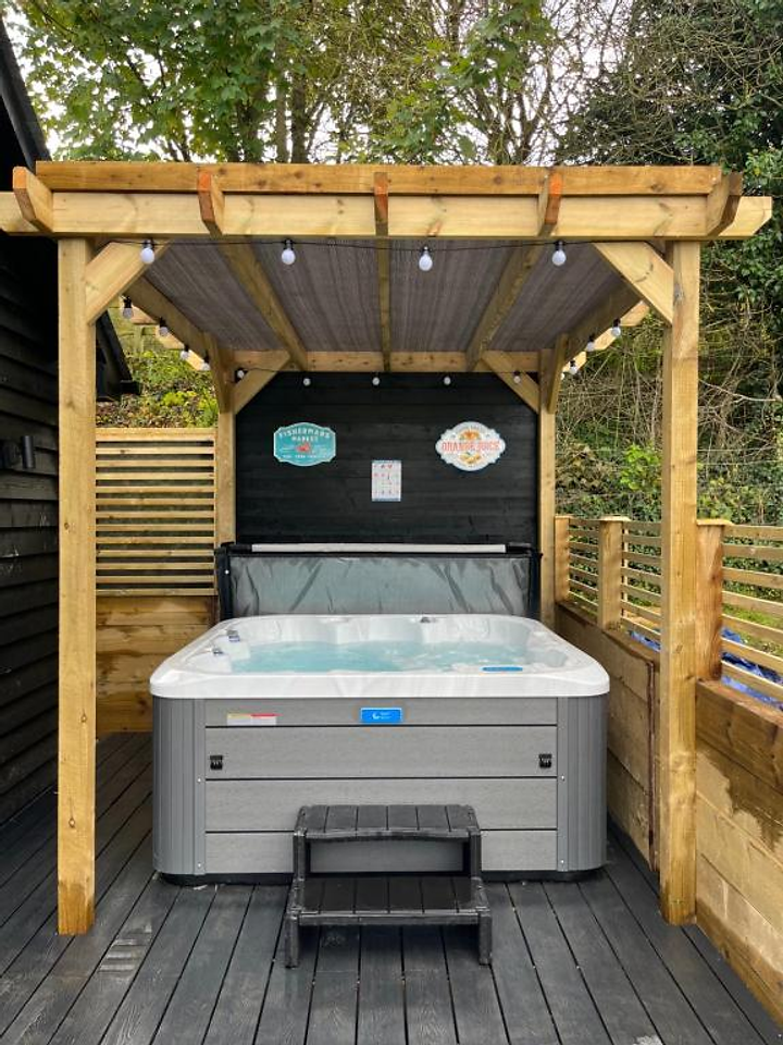 Private hot tub beneath a wooden pergola with string lights at Lydden Bell Lodge
