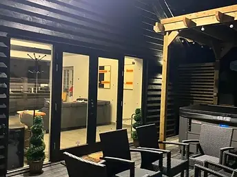 Lydden Bell Lodge illuminated exterior and wooden terrace with outdoor chairs after dusk