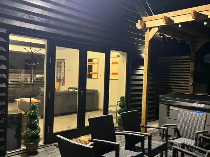 The Lydden Bell Lodge exterior with black timber cladding, a deck and illuminated French doors at dusk