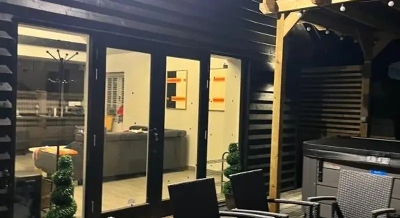 Exterior of Lydden Bell Lodge at dusk, with lit patio doors and outdoor dining furniture on the wooden terrace