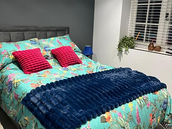 Double bedroom with turquoise floral bedding, a navy throw and dark accent wall