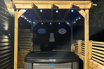 Lydden Bell Lodge hot tub covered at night beneath the timber pergola with colourful string lights