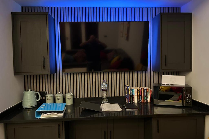 Media area at Lydden Bell Lodge with a wall-mounted television, charcoal slatted cabinetry and ambient lighting
