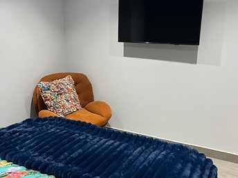 Double bedroom with colourful bedding, wall-mounted television and an orange armchair