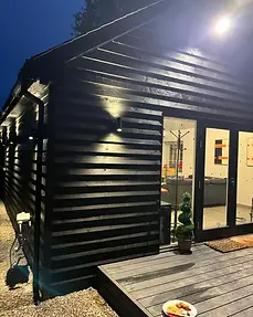 Evening photograph showing dark timber cladding and illuminated French doors of Lydden Bell Lodge