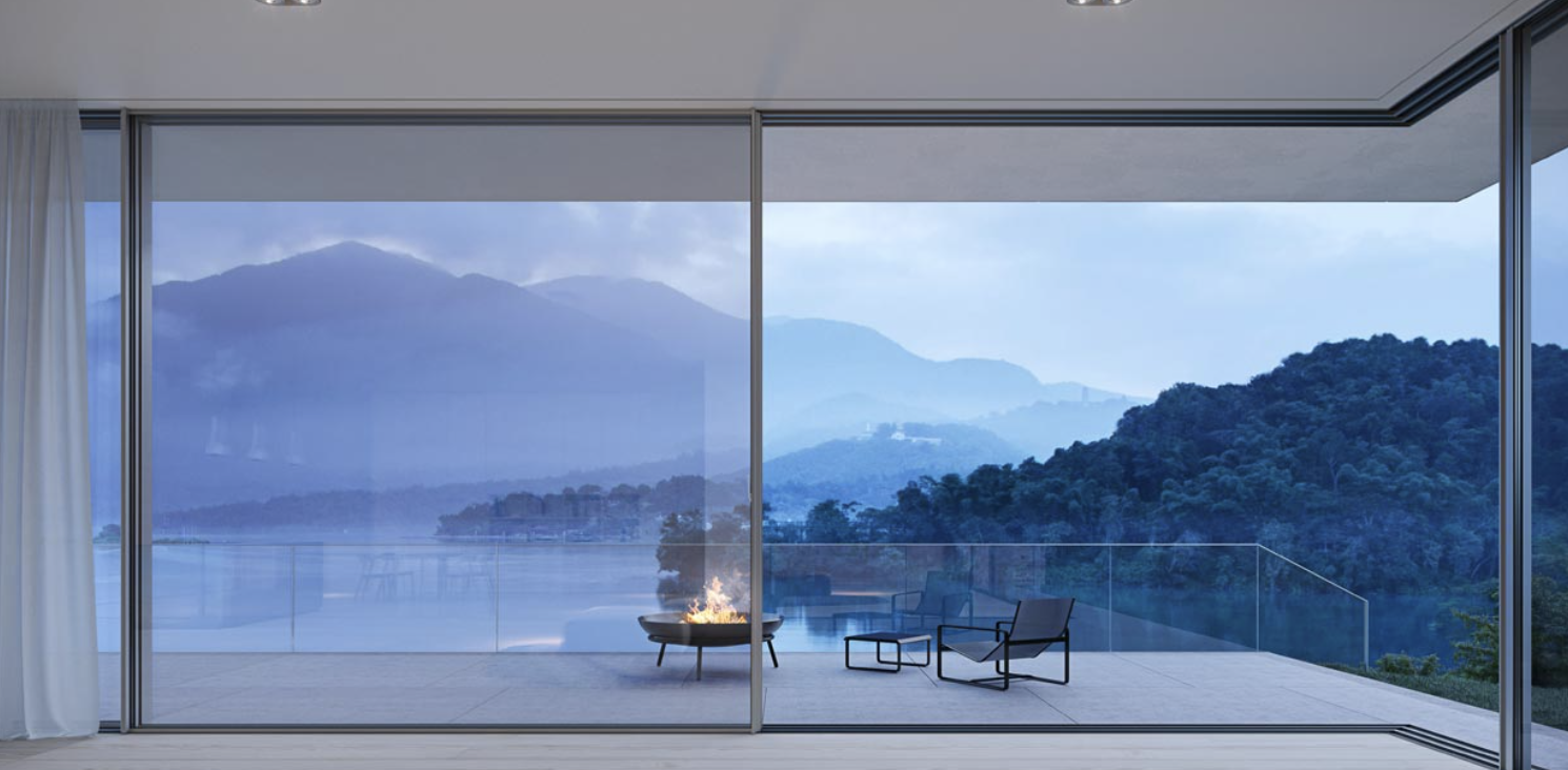 Looking through sliding doors to a terrace with a lit fire pit and a lake at dusk