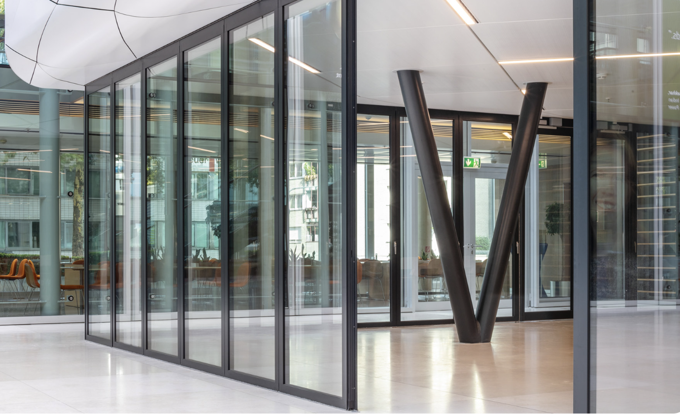 A horizontal sliding wall of glass panels on a floor track beside a V-shaped column in an office interior