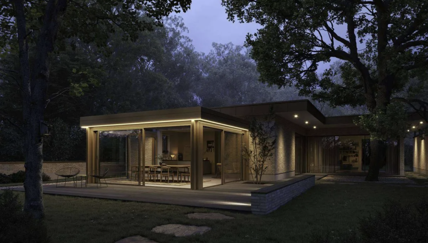 A flat-roofed glass extension on a brick house at dusk, its sliding doors open and lighting washing down the glass above a timber deck