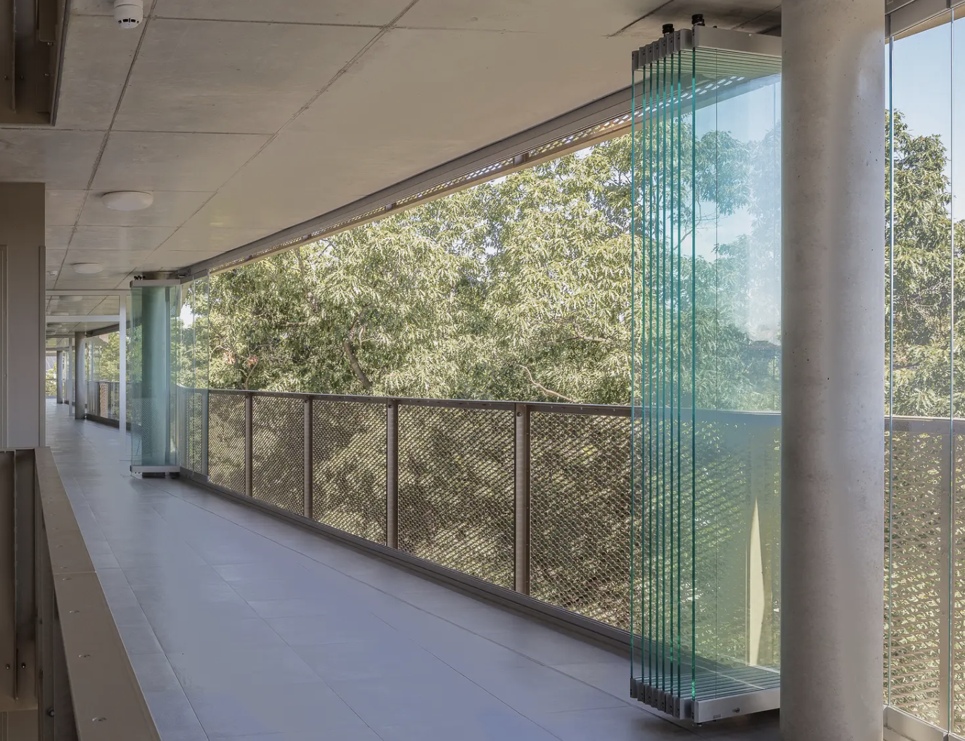 A covered balcony walkway with the sliding panels parked open beside a concrete pillar and mesh railing