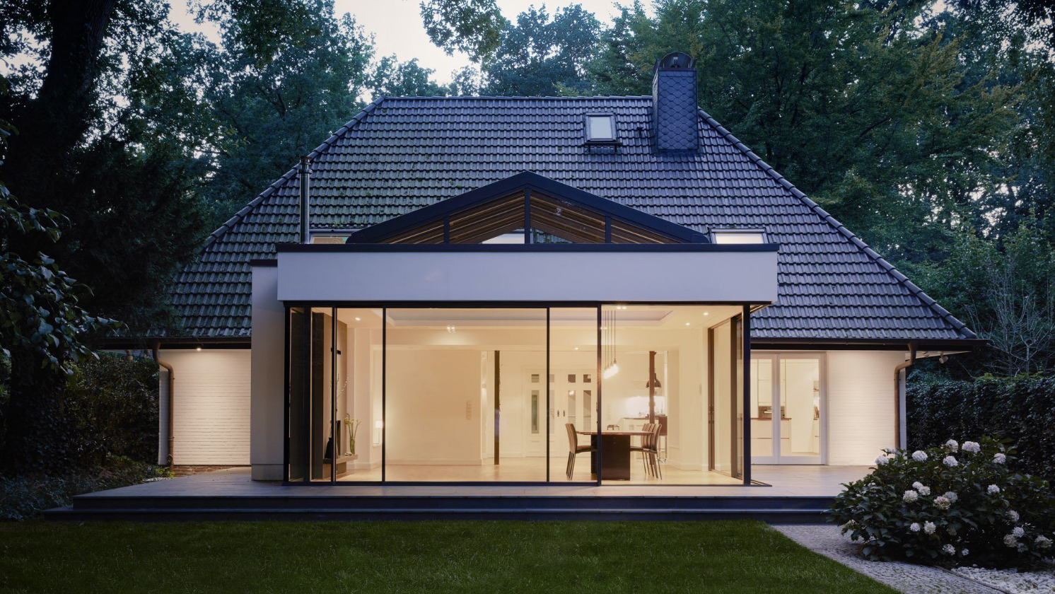 Floor-to-ceiling sliding doors lighting a tiled patio and lawn at dusk