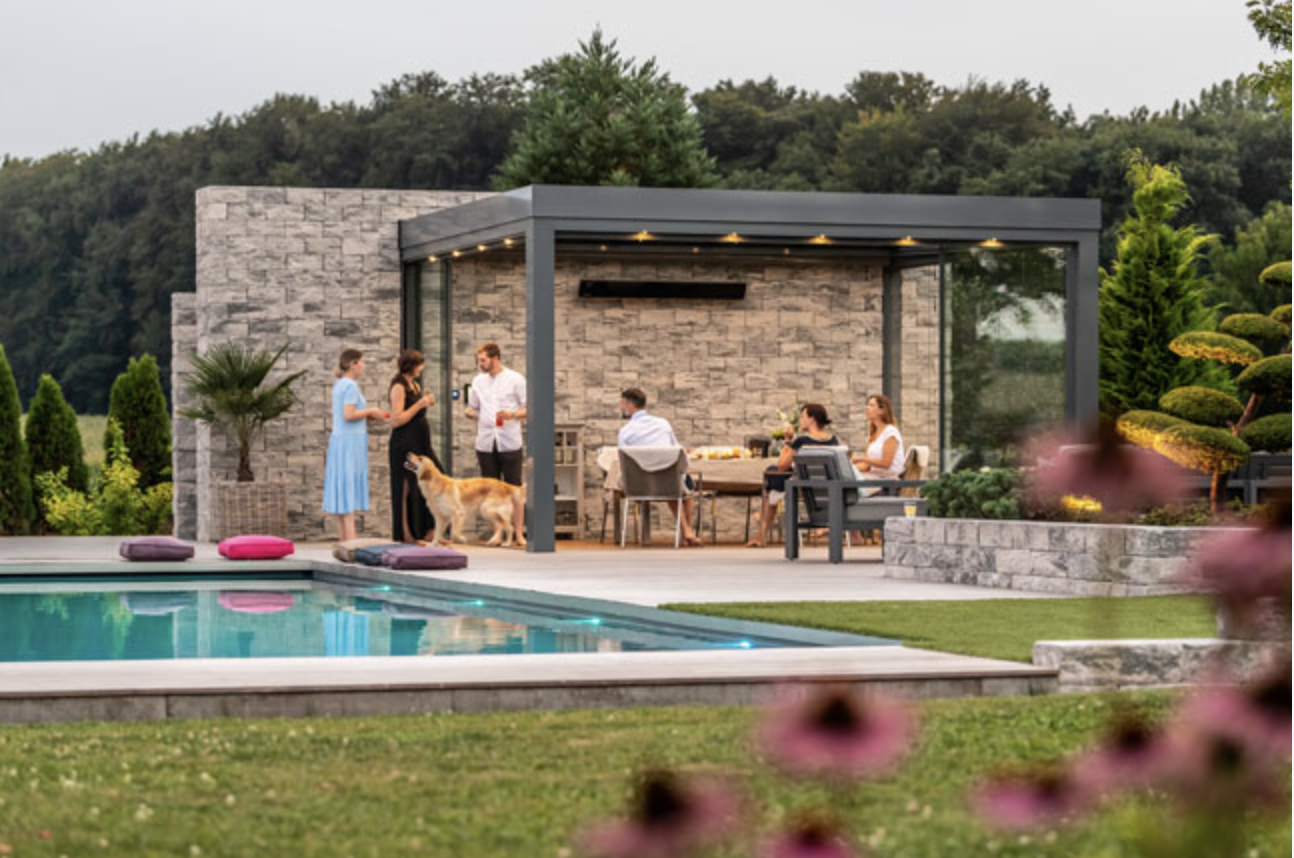 A glass canopy over a poolside dining table with guests seated, the pool and planting in the foreground