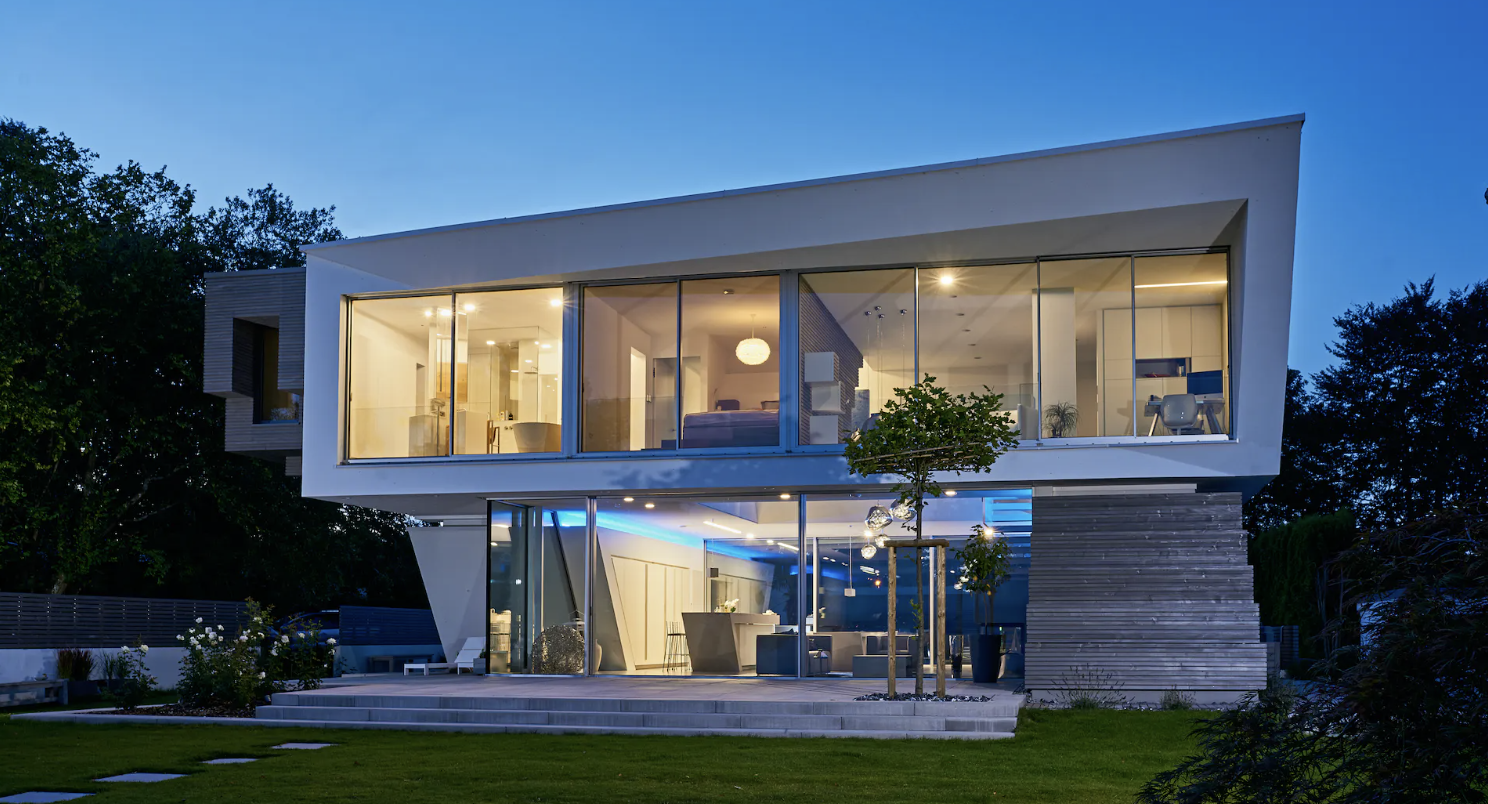 A two-storey house at twilight with sliding doors lighting the ground-floor living space