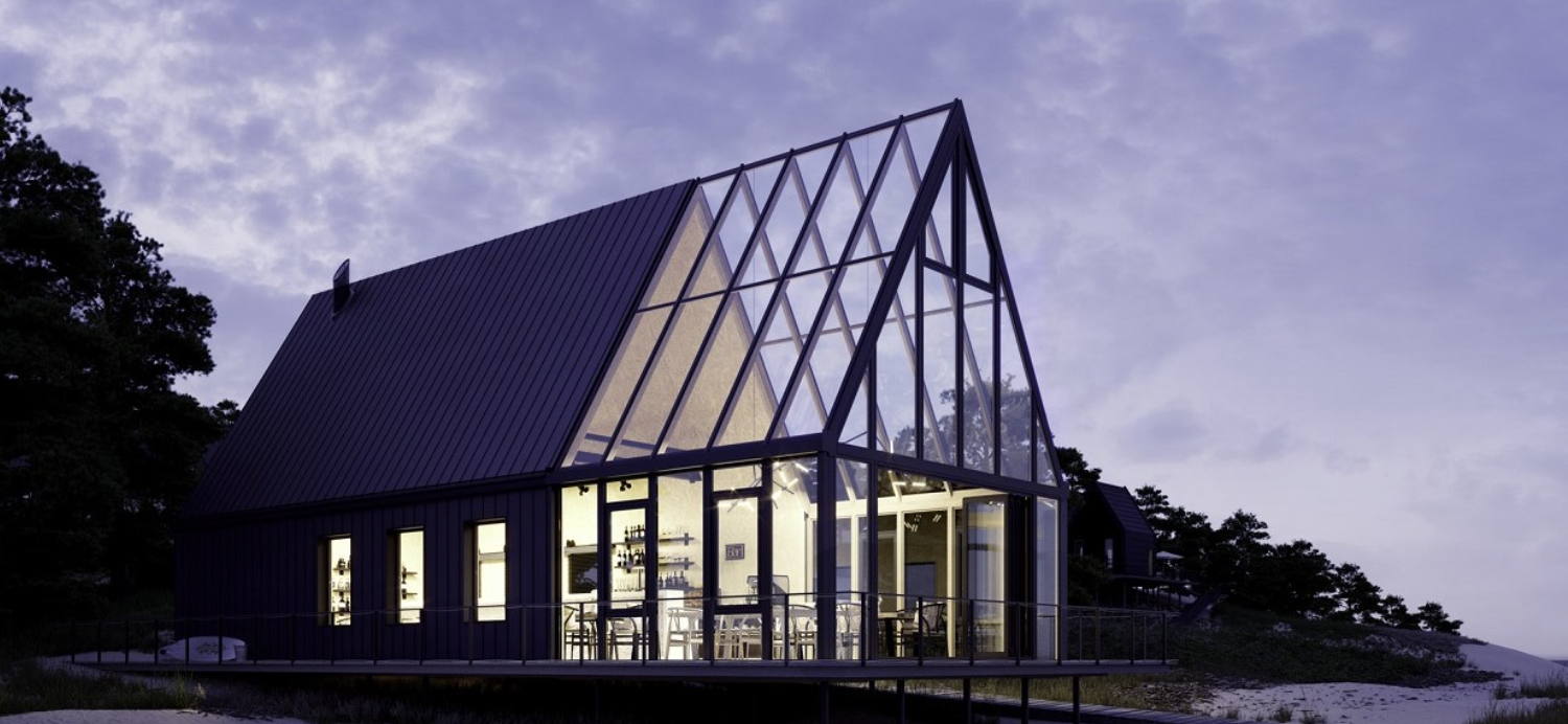 A gabled wintergarden at dusk, its clad roof running into glass above a lit bar and dining area on a raised coastal deck