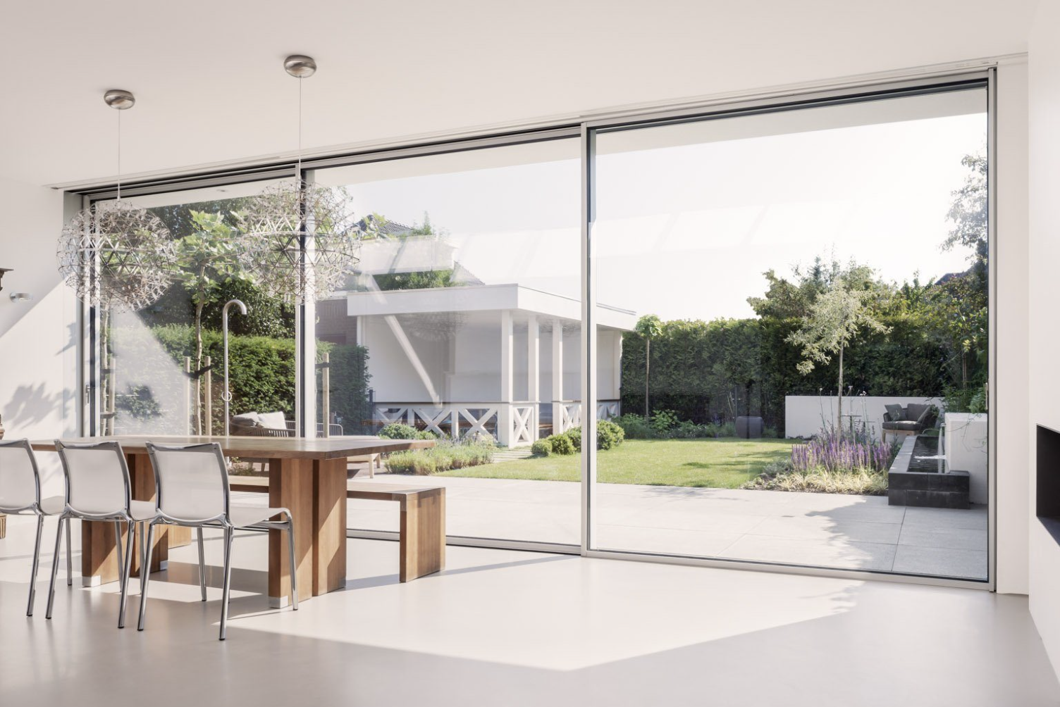 A dining space behind a sliding glass wall, open onto a lawn and water feature