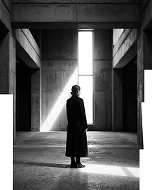 Figure in a dark coat silhouetted in a shaft of light inside a concrete gallery