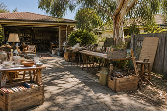 Trestle tables of secondhand household goods and vintage crates on a sunlit driveway