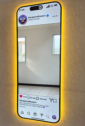 Espelho instagramável em formato de celular exibindo o perfil do Instagram do estabelecimento, com moldura preta e LED âmbar