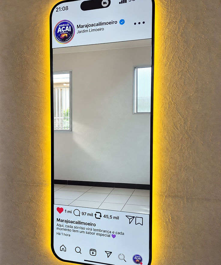 Espelho instagramável em formato de celular exibindo o perfil do Instagram do estabelecimento, com moldura preta e LED âmbar