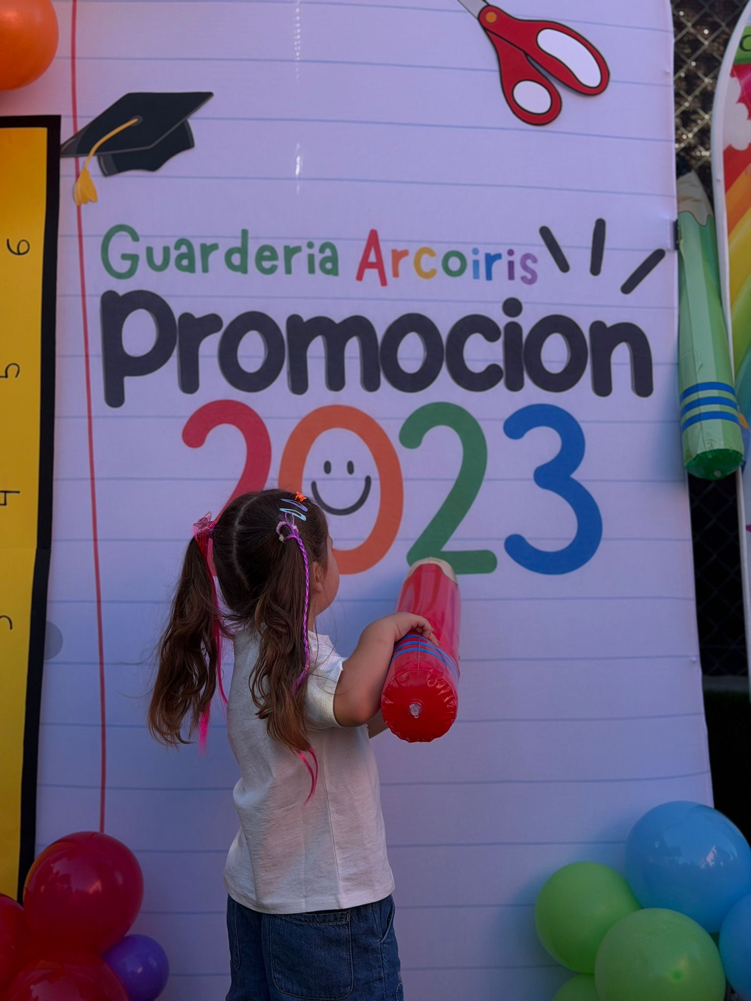 Niña con coletas sujetando un lápiz gigante frente al photocall