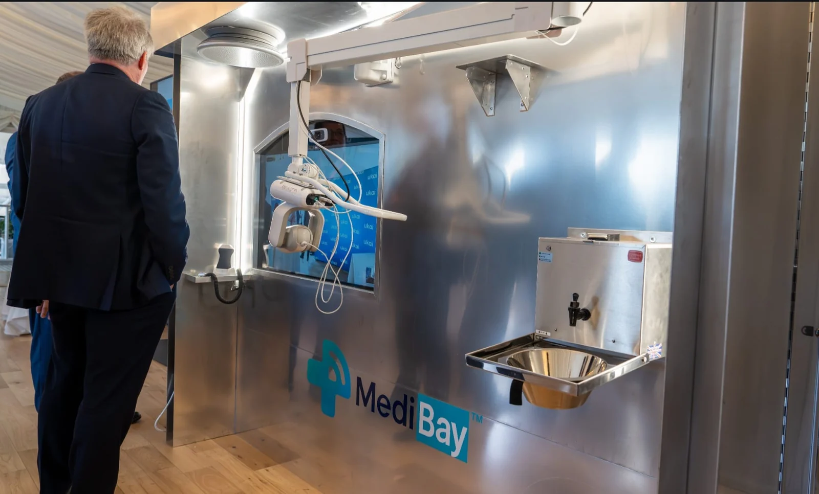 Wide original photograph of the MediBay TechWall at a demonstration, showing its screen, camera arm and workstation.