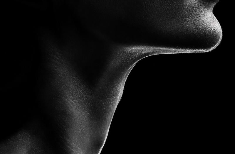 Black and white macro portrait of a jawline and neck emerging from deep shadow