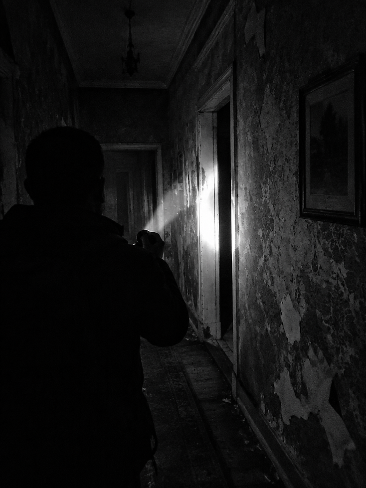 An investigator sweeping a darkened historic corridor with a flashlight