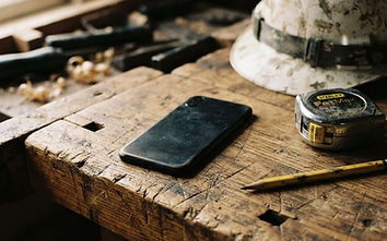 A smartphone on a workbench beside a tape measure and a hard hat