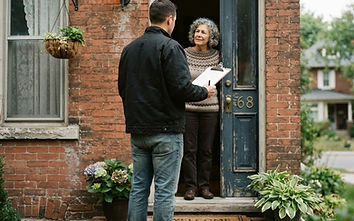 A contractor at a homeowner's front door holding a clipboard mid-conversation