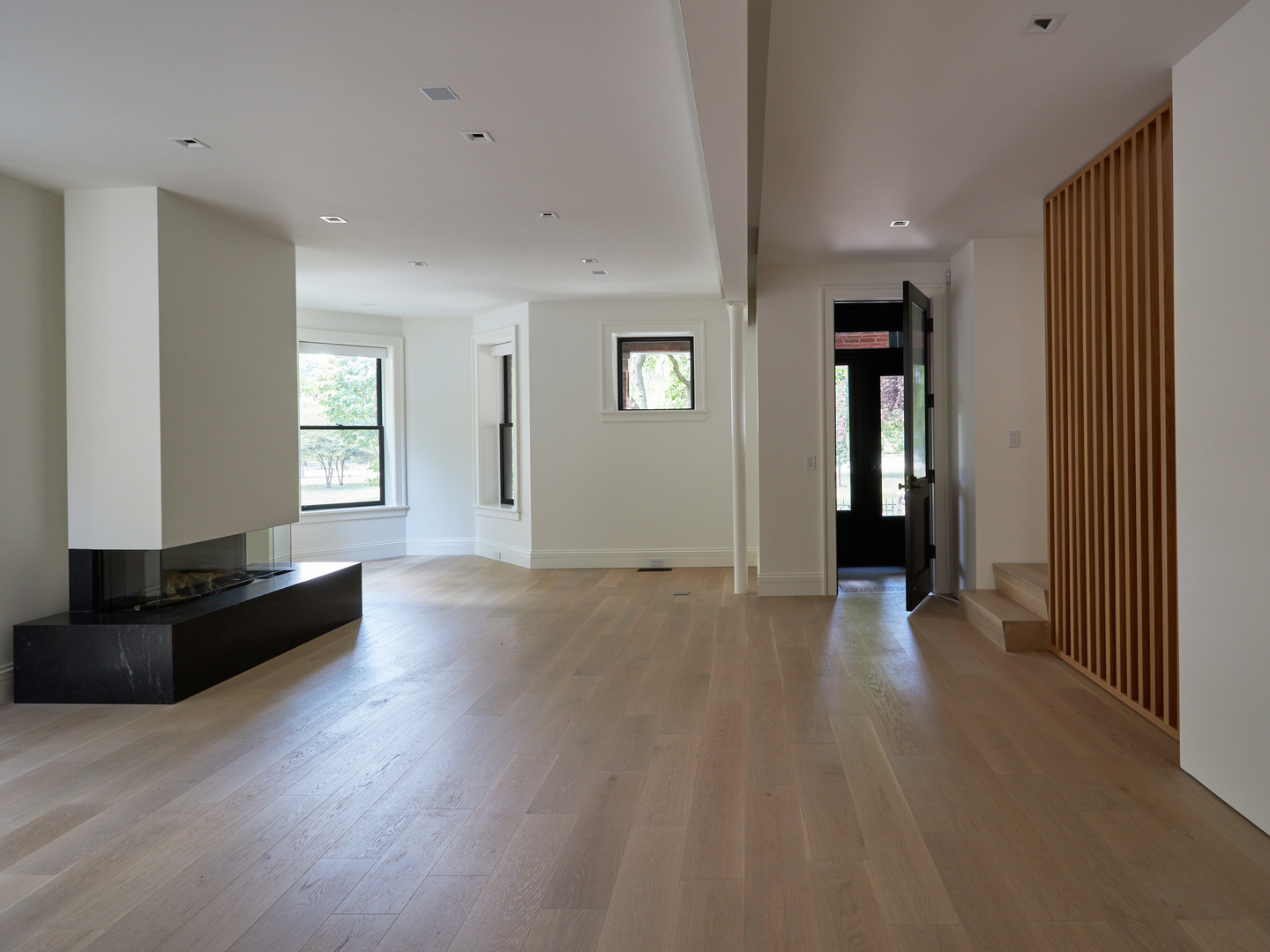 The living room from the front door: white oak floors, the linear fireplace and the slatted oak stair screen
