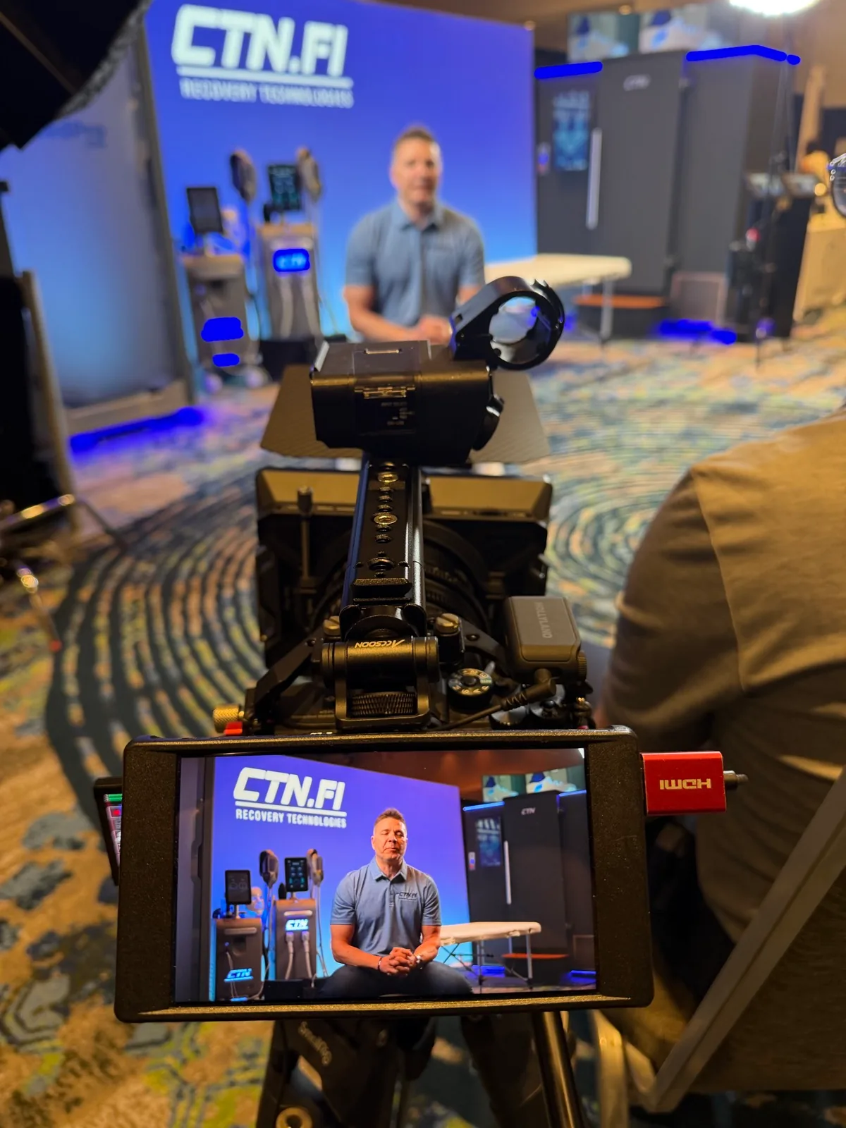 Cinema camera and monitor framing an interview in front of a CTN.FI display.