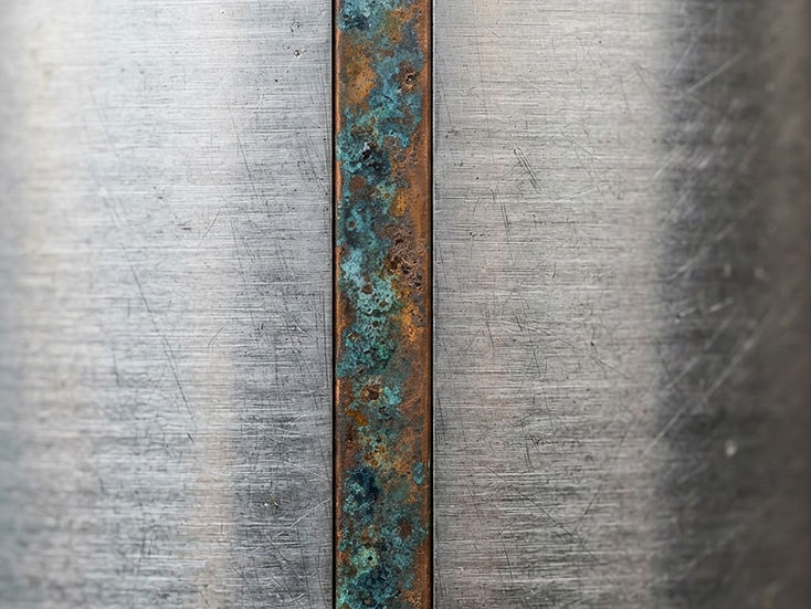 Makroaufnahme einer gebürsteten Aluminiumfläche mit einer Kante aus Kupfer