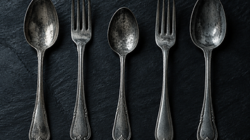 Vintage tarnished silver cutlery laid in a row on dark slate