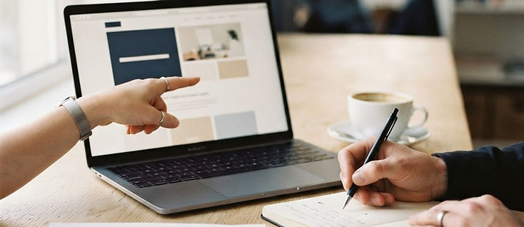 A website layout being reviewed on a laptop beside a notebook of handwritten notes