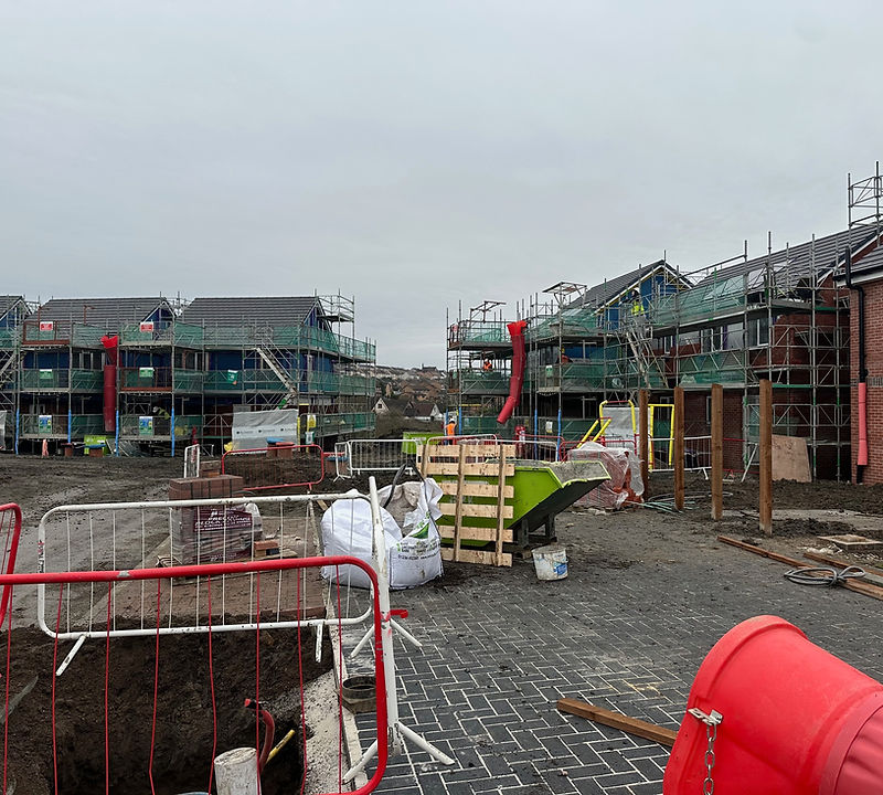 Scaffolded residential blocks during construction works, with site delivery and waste management in progress