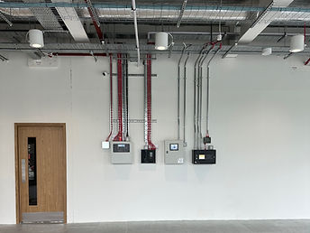 Wall-mounted control panels beside containment and fire pipework in a completed services area