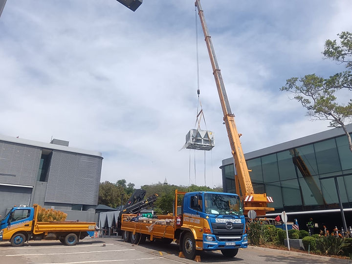 Consolidated crane lifting an industrial unit onto a flatbed truck outside an office building