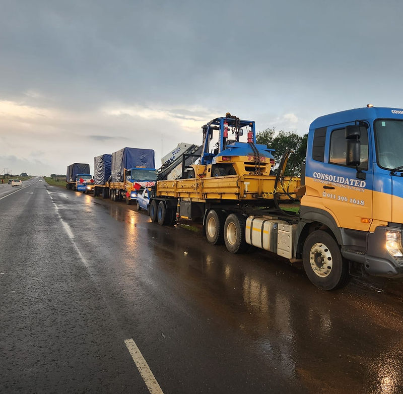 Convoy of Consolidated Investments trucks carrying abnormal loads on a highway at dusk