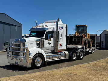 White Kenworth truck on a low loader trailer carrying a yellow loader