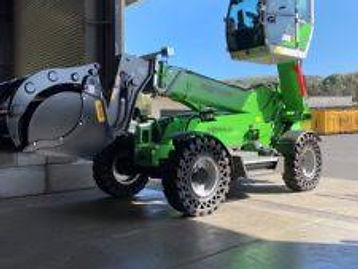 Green telehandler with a grab attachment inside an open shed