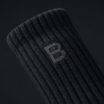 Extreme close-up of black ribbed sock fabric with the geometric B knitted into the cuff in tonal charcoal yarn