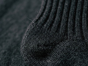 Macro photograph of a black knitted sock heel showing dense reinforcement stitching