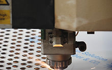 Cabezal de corte láser CNC cortando placa de acero con chispas en el taller