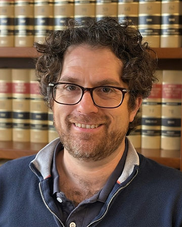 Marshall Kleiber smiling in glasses and a dark blue zip-up sweater in front of a bookshelf
