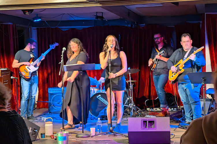 The five-piece band mid-song in front of red velvet curtains, blue stage lights on the floor