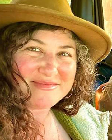 Tiana Cicco in a wide-brimmed felt hat, smiling off-camera in soft sunlight