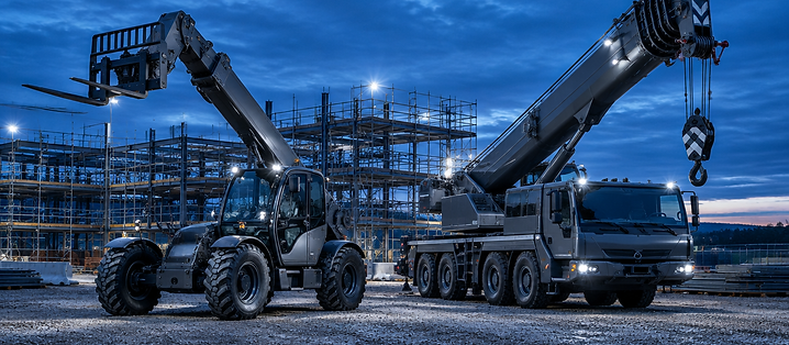 Teleskoplader und Autokran auf einer Baustelle bei Dämmerung
