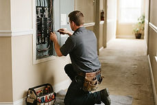 Maintenance technician working at an open electrical panel in an apartment hallway
